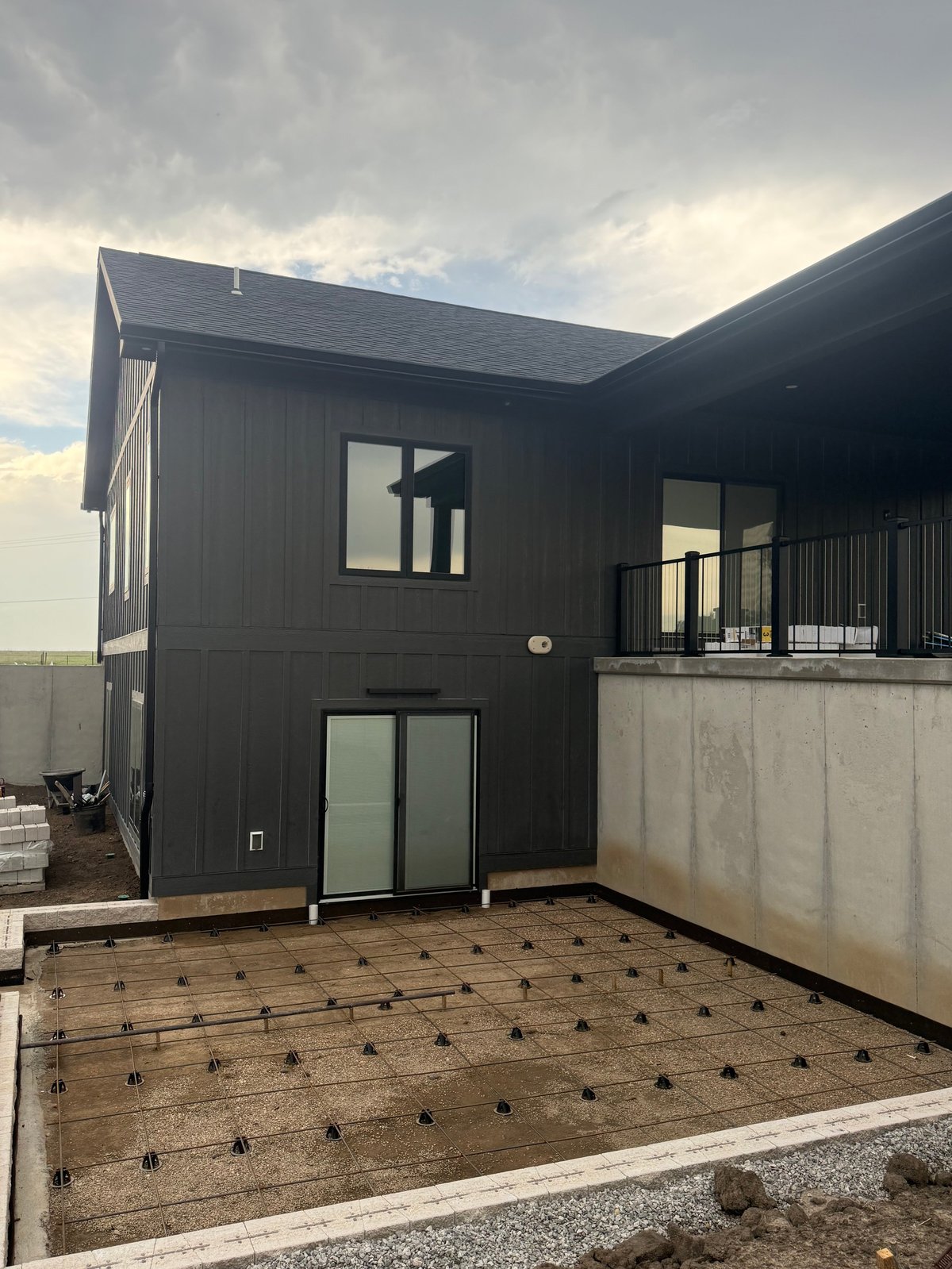 Modern dark-colored residential building with metal siding and concrete foundation under construction with exposed wooden framing in foreground