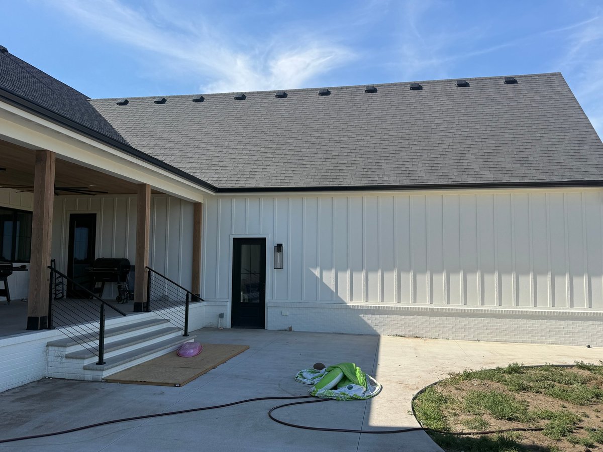 Modern white barn-style building with metal siding, covered porch entry, and black roof under blue sky