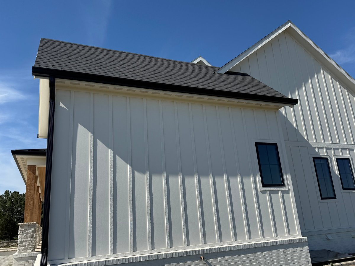 Modern farmhouse with white vertical siding, dark roof, and blue sky