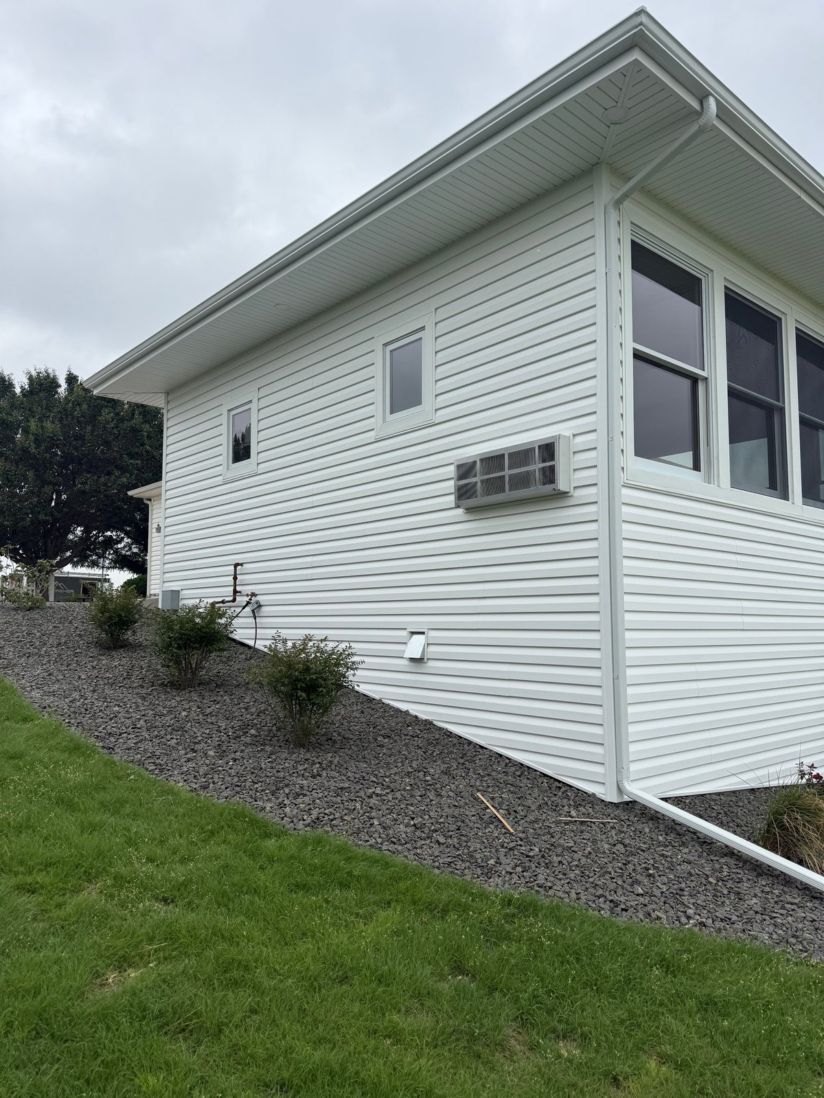 White horizontal siding house with pitched roof, multiple windows, and landscaped yard with grass and gravel foundation planting