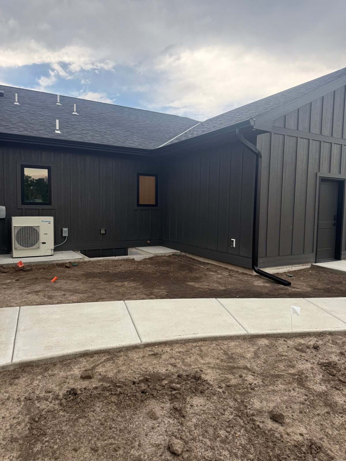 Modern black metal-sided building exterior with angled roof, concrete patio, and HVAC unit under construction