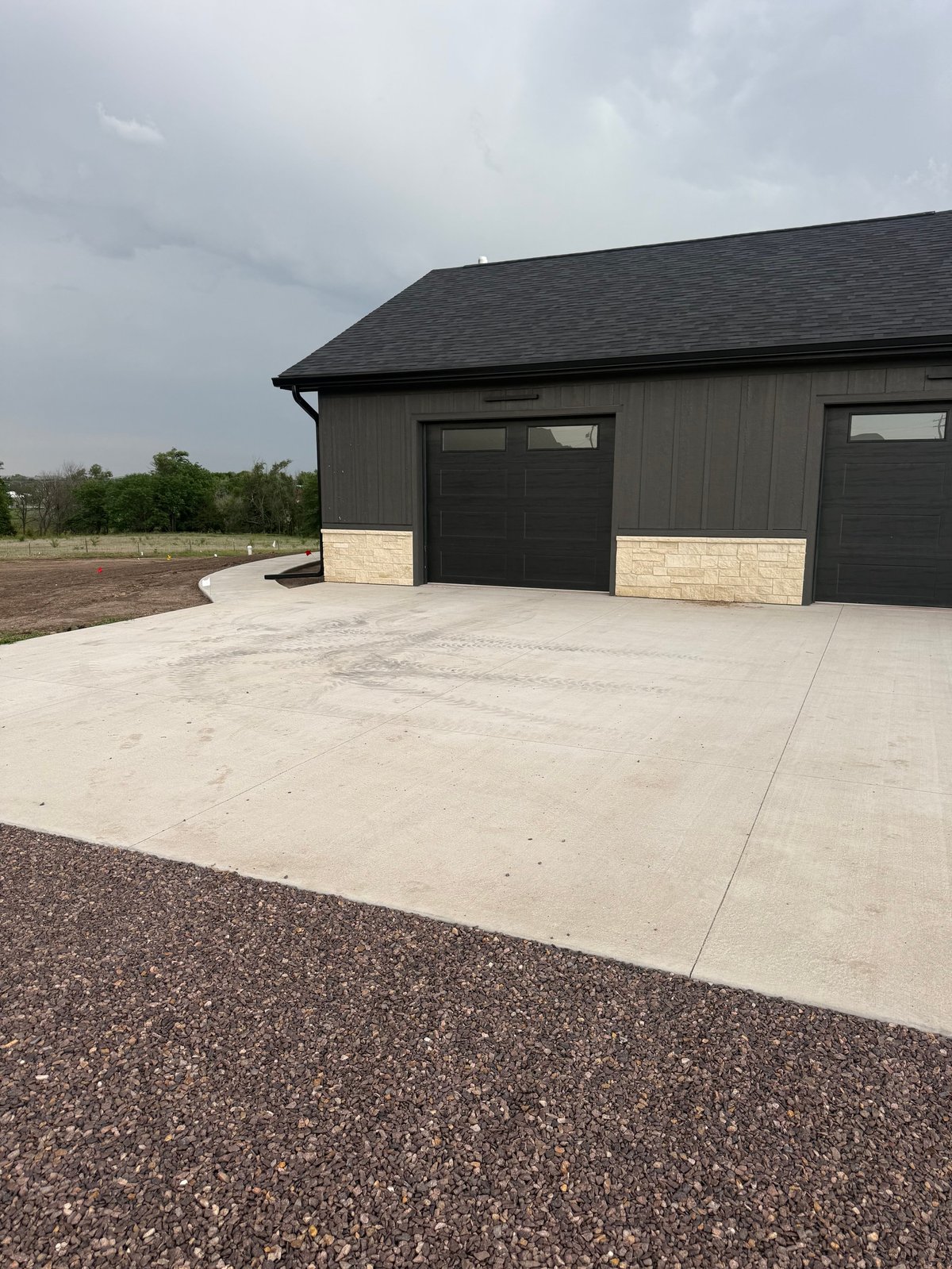 Modern black garage with two doors on concrete driveway, overcast sky and rural landscape background