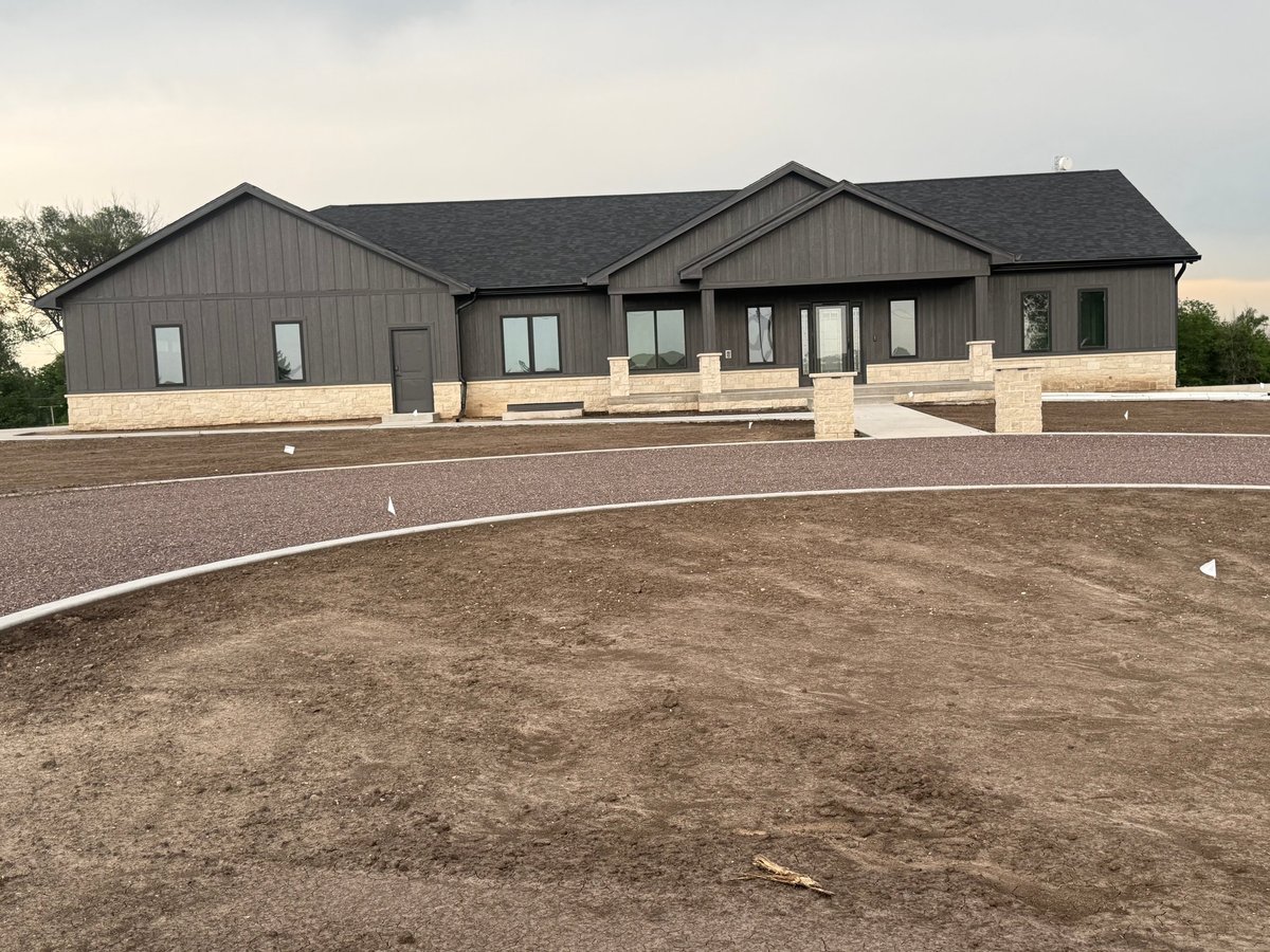 Modern gray residential home under construction with curved driveway and landscaping stones visible in front yard