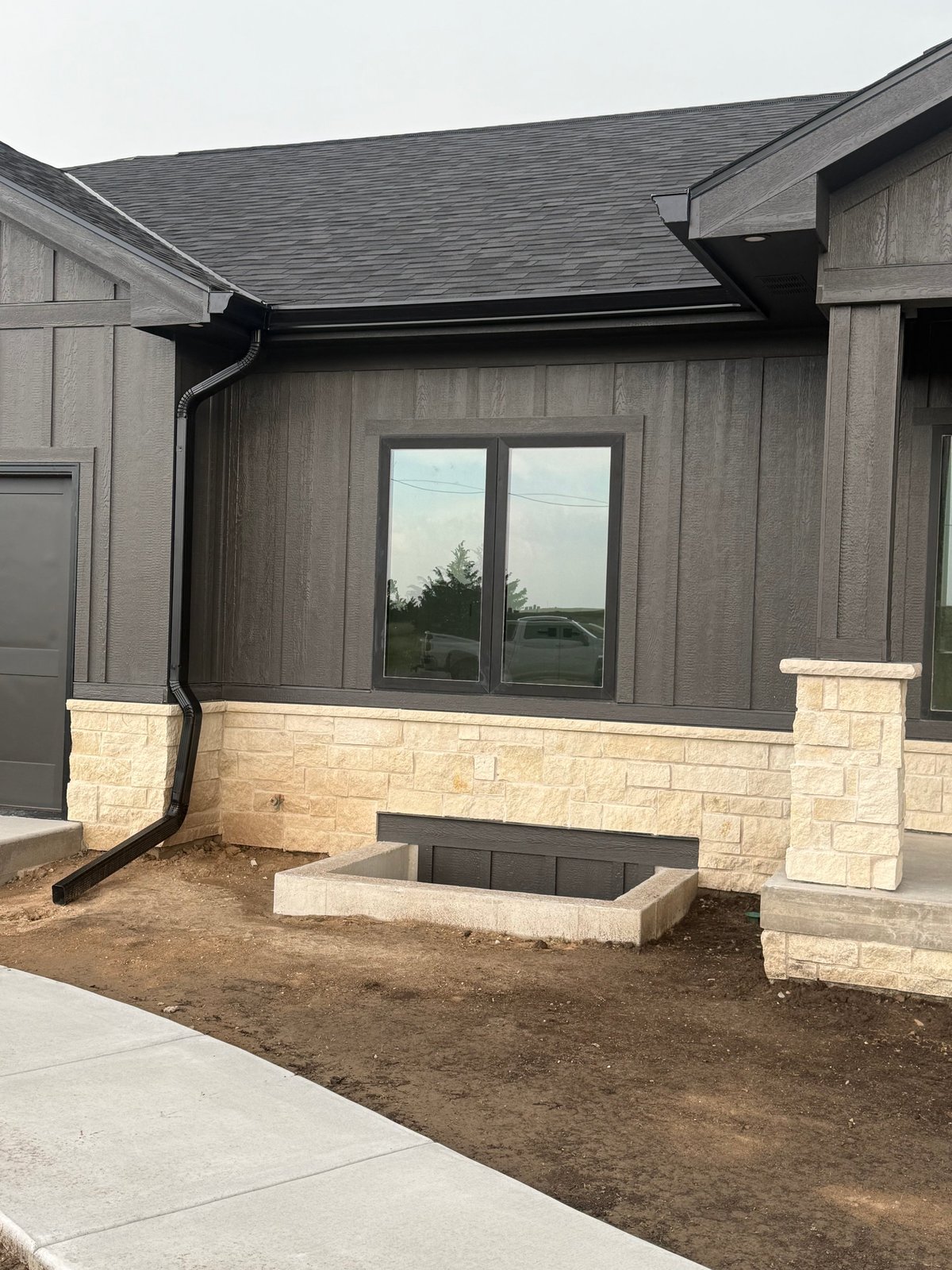 Modern home exterior with gray siding, stone foundation, double windows, and landscaping under construction