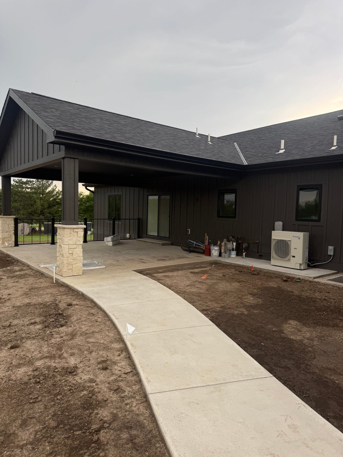 Modern black house with metal roof and concrete patio, surrounded by bare landscaping and gravel yard