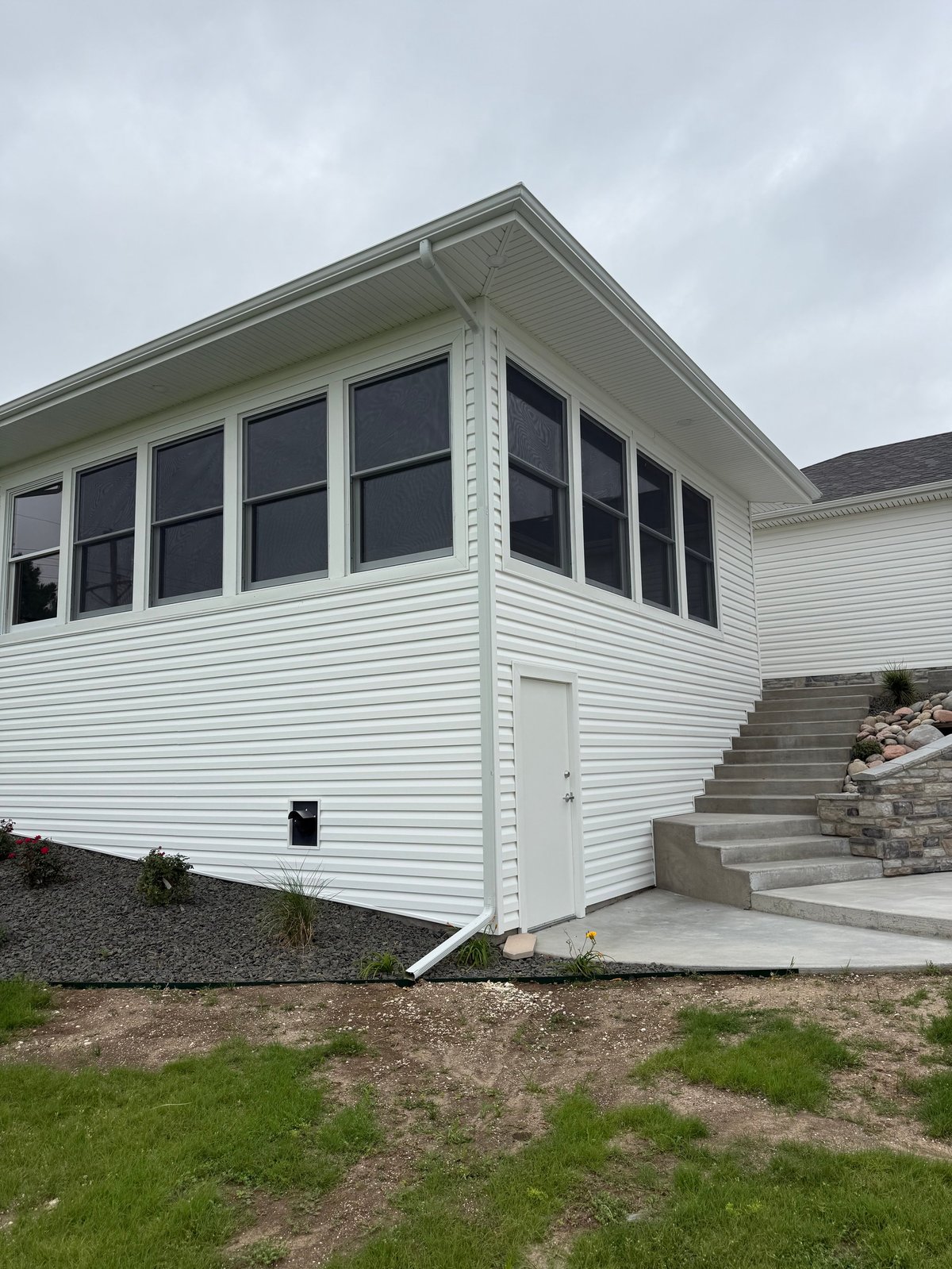 Modern white house addition with large windows, concrete steps, and landscaping under cloudy sky