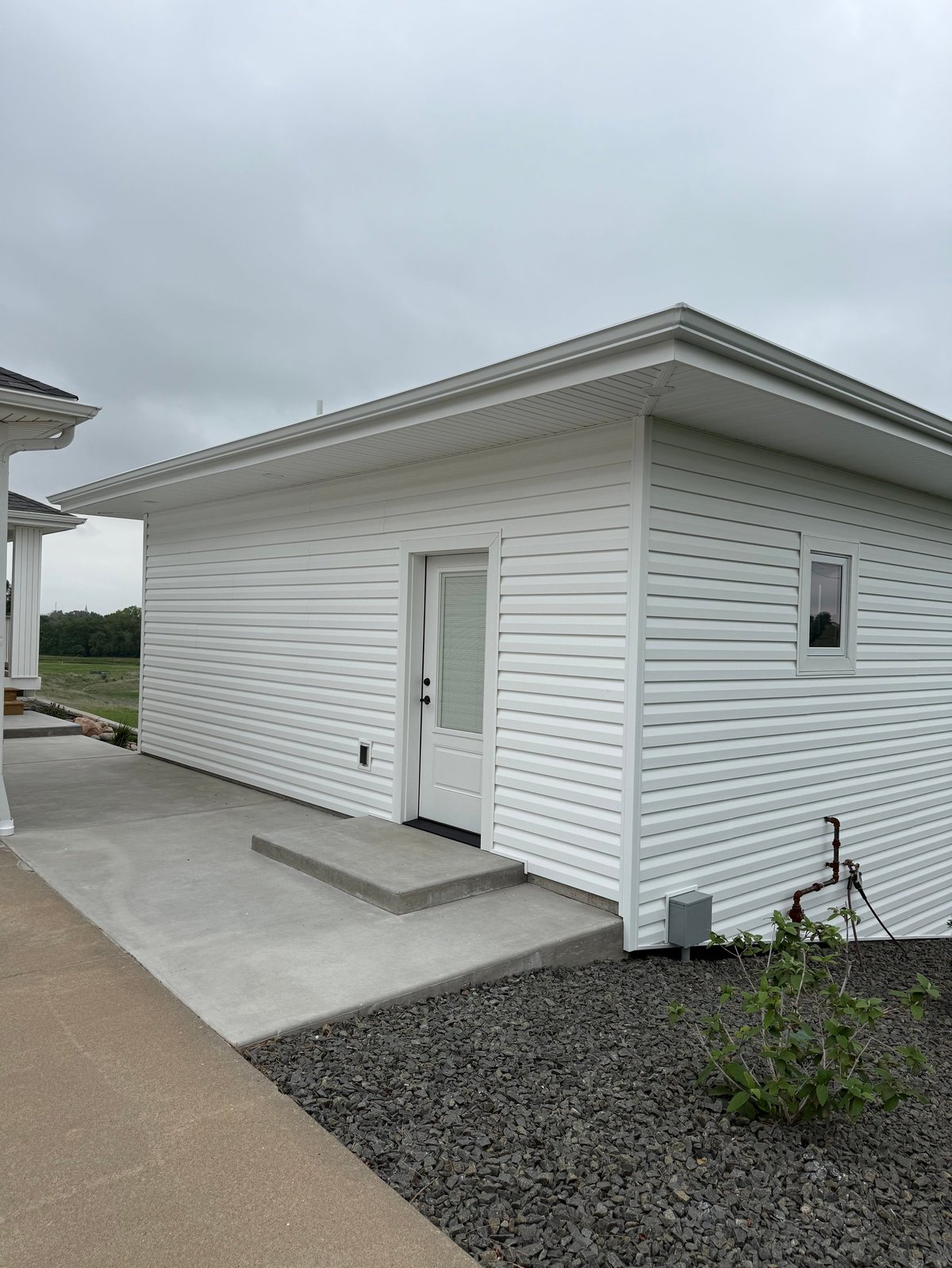 White residential building with horizontal siding, concrete patio, and landscaping under overcast sky