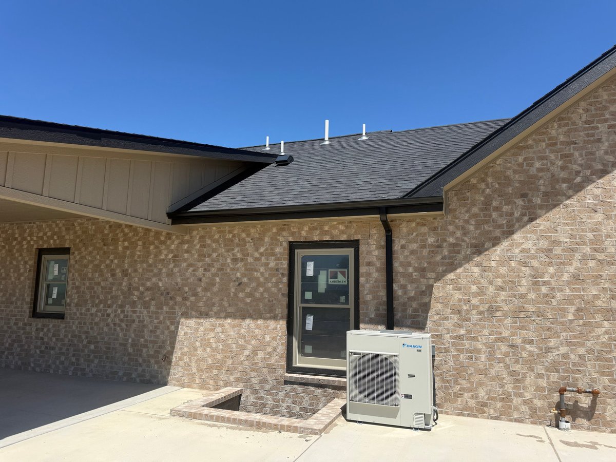 Modern brick home exterior with HVAC unit mounted on wall beside dark entrance door under clear blue sky