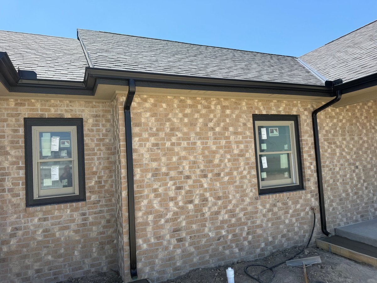 Exterior of brick building with two windows, gutters, and drainpipes under clear blue sky