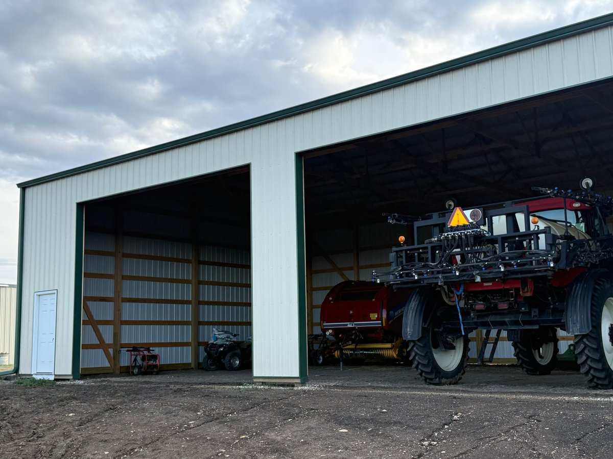 Large metal agricultural storage building with two open bays, one containing a truck and the other with shelving