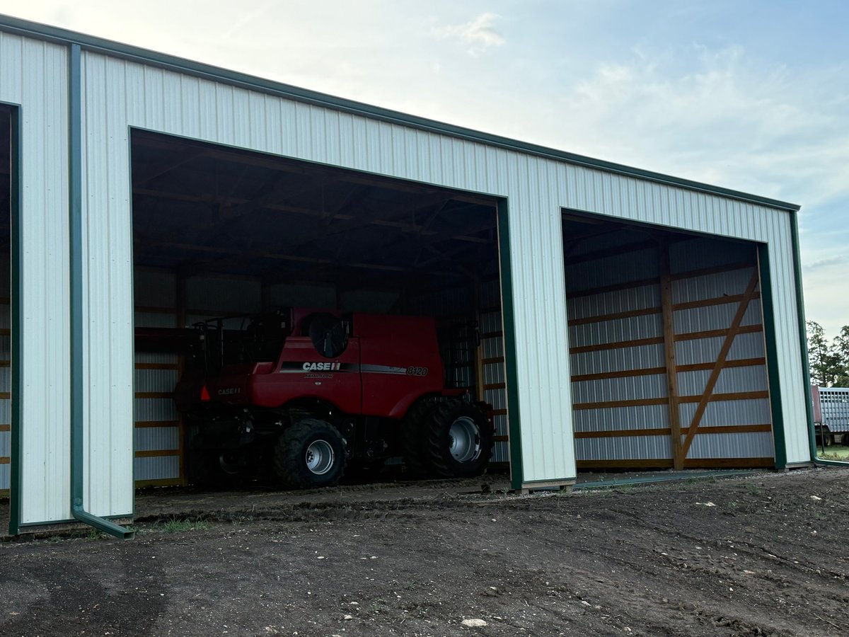 Red combine harvester parked inside a metal agricultural storage building with open garage doors