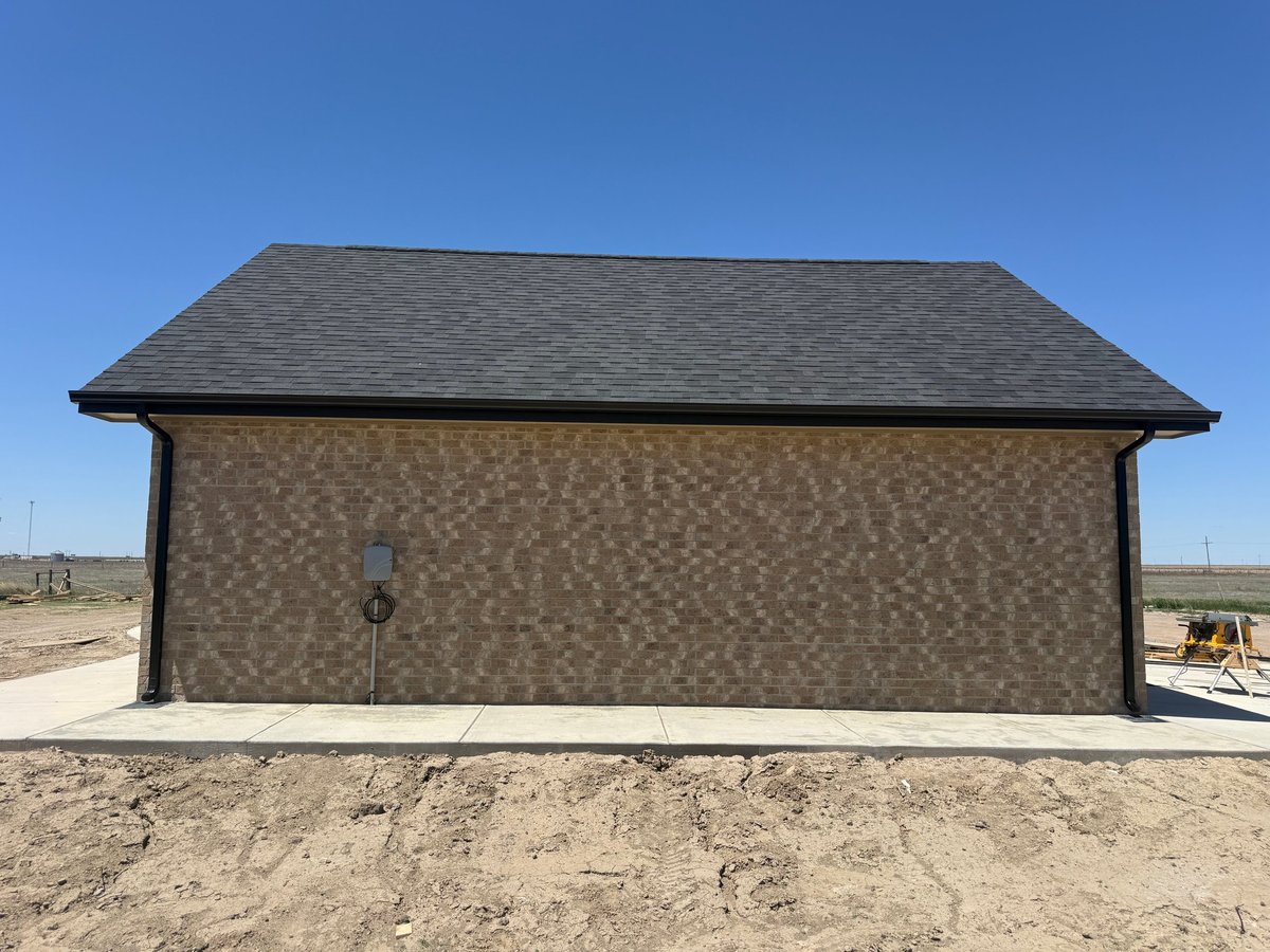 New construction garage with black roof and brown brick facade on sandy desert lot under clear blue sky